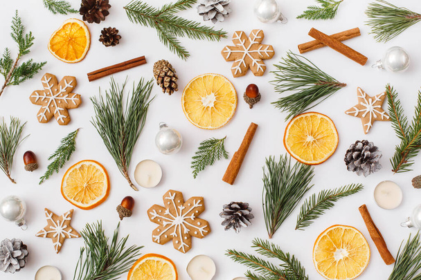 Christmas, winter, new year composition. Pattern made of Fir tree branches, pine cone, dried oranges, cinnamon sticks, gingerbread, candles on white background. Flat lay, top view, copy space - Foto, afbeelding