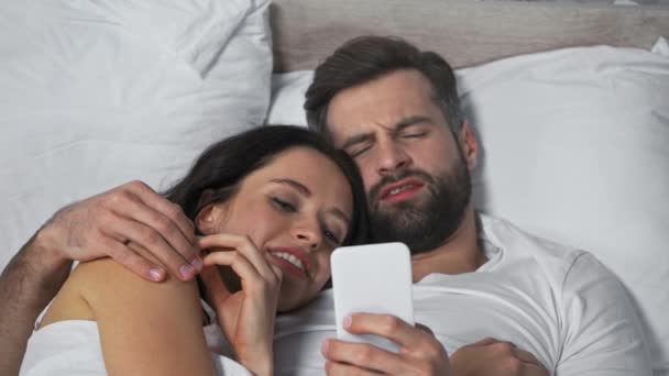 focus pull of couple lying in bed and looking at smartphone  - Footage, Video