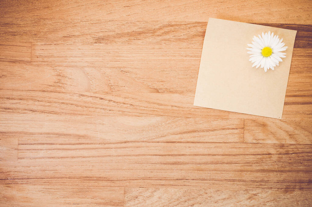 A high angle shot of a Daisy flower and a piece of paper on a wooden surface - 写真・画像