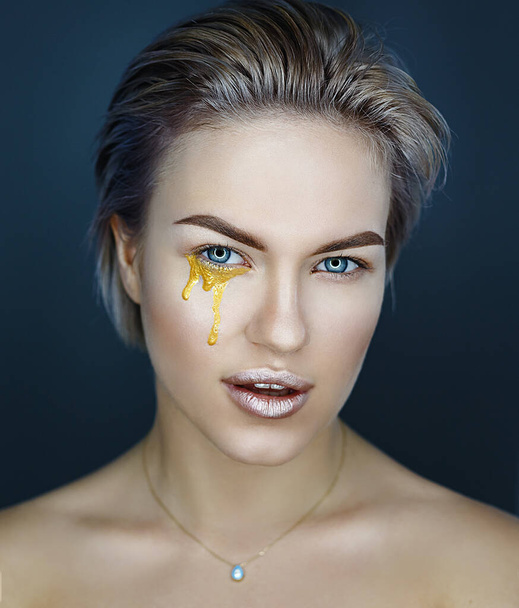junges weibliches Gesicht mit goldenem artistischem Make-up, Blick in die Kamera, Tränen, Nahaufnahme von vorne - Foto, Bild
