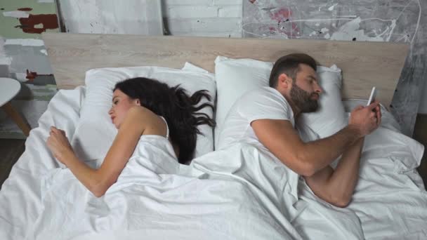 Hochwinkelaufnahme eines Paares, das im Bett liegt und auf Smartphones SMS schreibt - Filmmaterial, Video