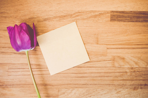A high angle shot of a purple tulip and a piece of paper on a wooden surface - copy space - Foto, Bild