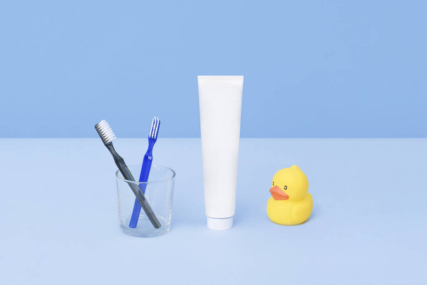 Toothbrushes and tube of toothpaste with rubber yellow duck on blue background. Teeth hygiene concept. Flat lay. Natural beauty products for branding mockup concept. Add your text. - Фото, изображение