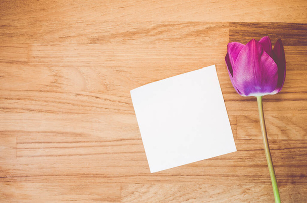 A high angle shot of a purple tulip and a piece of paper on a wooden surface - copy space - Valokuva, kuva