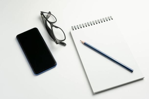 鉛筆、スマートフォン、眼鏡を背景にしたノートブックのトップビュー。ビジネス、ワークスペース、テクノロジーライフスタイルのコンセプト - 写真・画像