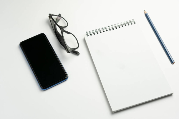 Top pohled na notebook s chytrým telefonem a brýlemi na bílém pozadí.Byznys, pracovní prostor, koncept technologického životního stylu - Fotografie, Obrázek