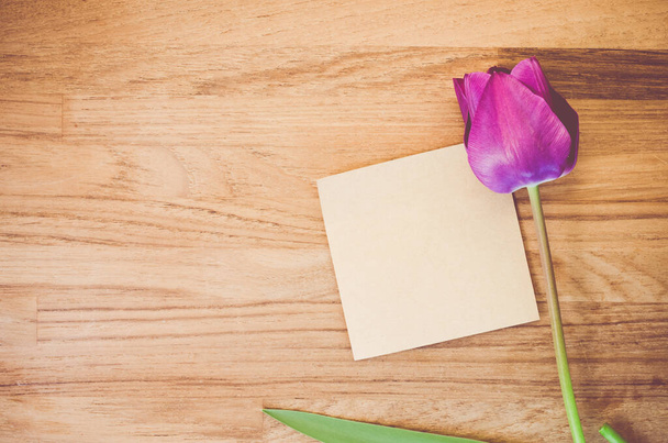 A high angle shot of a purple tulip and a piece of paper on a wooden surface - Φωτογραφία, εικόνα