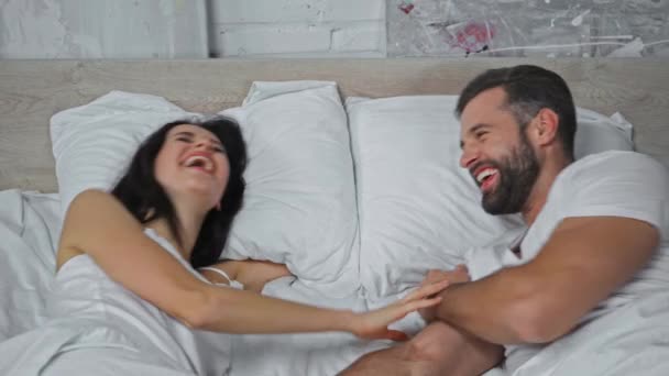 幸せな若いカップルがベッドルームで話して笑っています  - 映像、動画