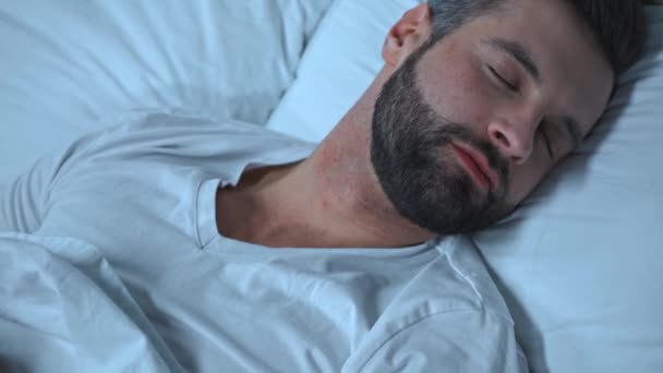 brodaty młody człowiek śpiący w łóżku w domu - Materiał filmowy, wideo