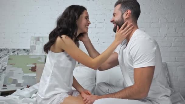 side view of happy woman touching face of boyfriend in bedroom  - Кадри, відео