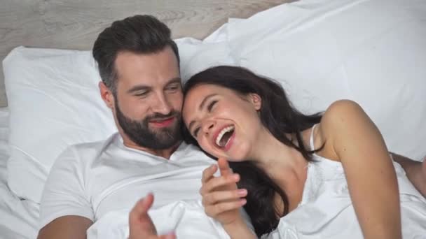 magas szög kilátás boldog férfi fekvő mosolygós barátnő az ágyban - Felvétel, videó