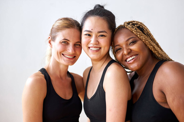 natural beauty concept. three diverse females in black sportswear smiling - Foto, imagen