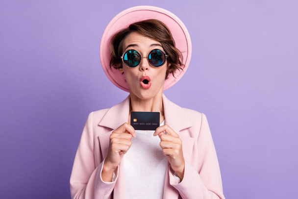 Photo of curly surprised woman wear casual pink vintage blazer sun spectacles holding wireless credit card isolated purple color background - Foto, immagini