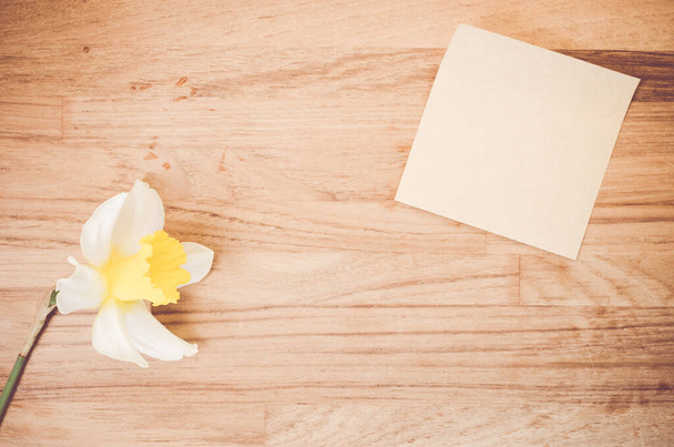 A high angle shot of a daffodil and a piece of paper on a wooden surface - copy space - Foto, imagen