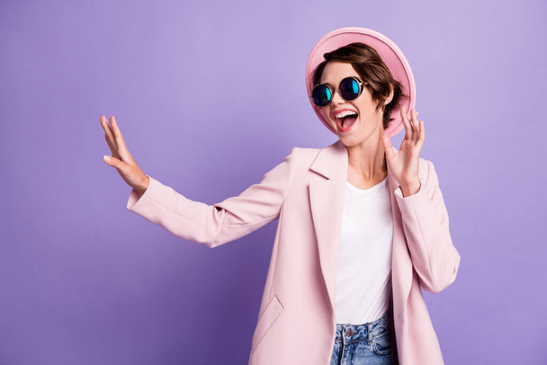 Photo of pretty optimistic young woman dancing wear coat cap glasses top look empty space isolated on purple color background - Fotó, kép