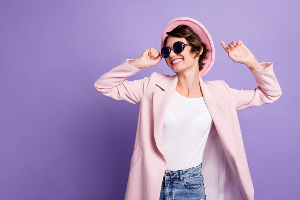 Photo of nice positive brunette hair young lady dance wear cap coat look empty space isolated on violet color background - Φωτογραφία, εικόνα