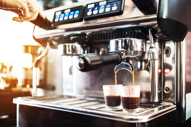 Κοντινό πλάνο χέρι barista εισάγει το μεταλλικό φίλτρο στη μηχανή του καφέ, περιμένοντας για χύτευση ζεστό μαύρο καφέ μέσα σε ποτήρια μέτρησης. Μαθήματα παρασκευής καφέ για επιχειρηματίες που ξεκινούν μικρές επιχειρήσεις.  - Φωτογραφία, εικόνα