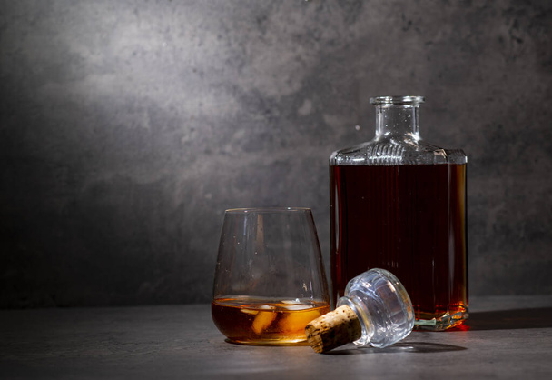 square whiskey bottle and glass with ice on dark gray cement background - 写真・画像
