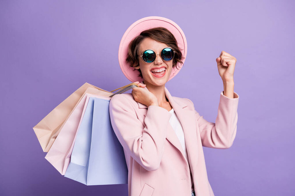 Portrait of hooray crazy sweet bob hairstyle young lady hold shoppers show fist wear pink cap coat isolated on purple background - Foto, imagen