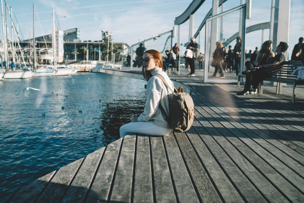 Beautiful female hipster tourist enjoying free day for promenade in harbor taking rest after walking near water dock, charming red hair traveler 20 years old recreating before voyage trip from dock - Φωτογραφία, εικόνα