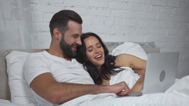 ευτυχισμένο ζευγάρι γελάει βλέποντας ταινία στο φορητό υπολογιστή στο κρεβάτι - Πλάνα, βίντεο