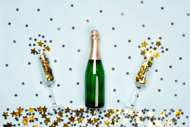 Bottiglia di champagne e flauti con stelle nere e dorate e coriandoli circolari sullo sfondo blu. Natale, Capodanno o compleanno o matrimonio concetto festivo. Vista dall'alto e posa piatta. - Foto, immagini
