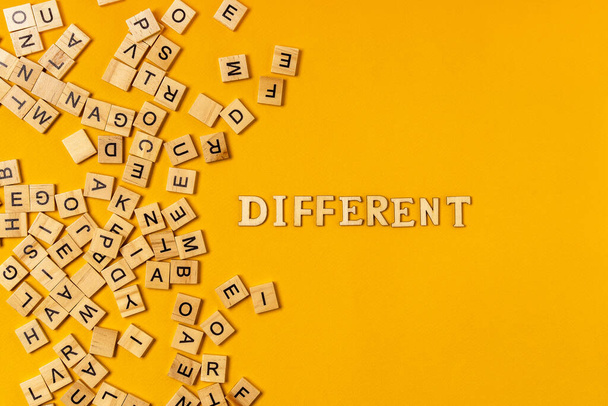 La palabra "DIFERENTE" está colocada sobre una mesa de letras de madera, junto a un montón de bloques de madera con letras. Concepto de personas con necesidades especiales - Foto, Imagen