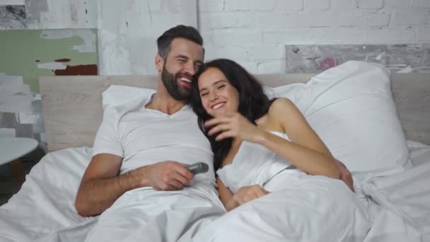 alegre pareja acostada en la cama y viendo comedia película - Imágenes, Vídeo