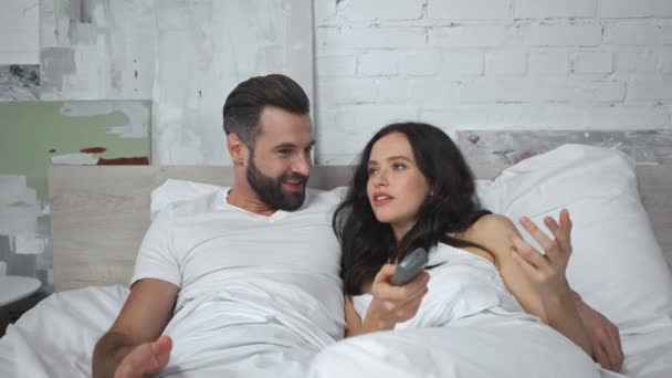 Mann nimmt unzufriedener Frau im Bett die Fernbedienung aus der Hand - Filmmaterial, Video