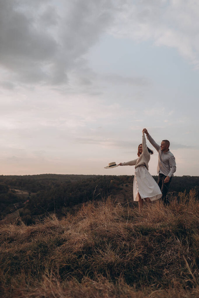 husband and his pregnant wife are walking at sunset in field on the outside. theme romantic pregnancy outdoors. - Foto, immagini