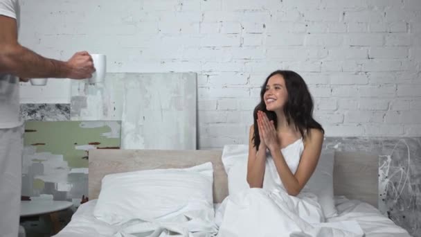 Mann gibt Tasse an glückliche Frau im Bett und schaut Film  - Filmmaterial, Video