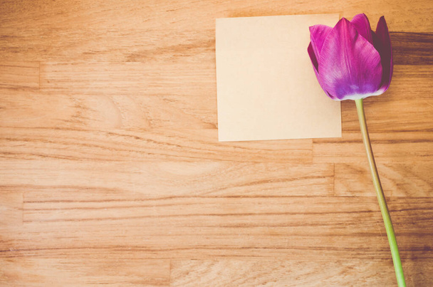 A high angle shot of a purple tulip and a piece of paper on a wooden surface - copy space - Foto, imagen