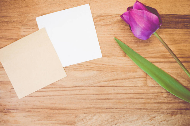 A high angle shot of a purple tulip and pieces of paper on a wooden surface - Foto, Imagen
