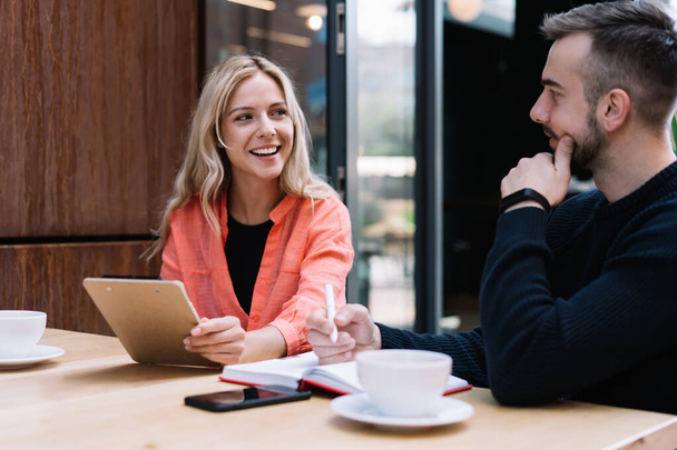 Cheerful caucasian female student looking a her male friend discussing learning project on cafe break, prosperous young man and woman employees talking to each other about business ideas on meeting - Фото, изображение