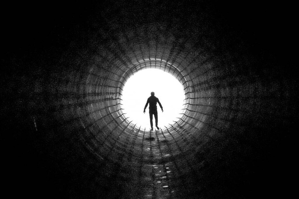 Η σιλουέτα ενός άντρα που περπατάει προς το φως στην άκρη ενός μεγάλου τούνελ. Έννοια της διαφυγής, εξόδου, ελευθερίας, κλινικού θανάτου - Φωτογραφία, εικόνα