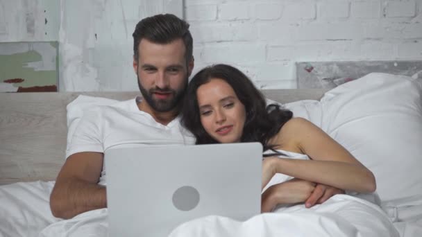 νεαρό ζευγάρι ξαπλωμένο στο κρεβάτι και βλέποντας κωμωδία στο laptop  - Πλάνα, βίντεο