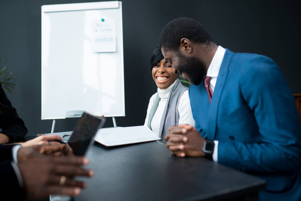 Two African American man and woman with a family business enter into a cooperation agreement. Sitting in an office next to a whiteboard - Foto, afbeelding