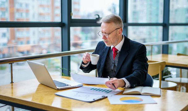 Thoughtful businessman reading important business papers, photo in front of the window with city view. Closeup. - Photo, image