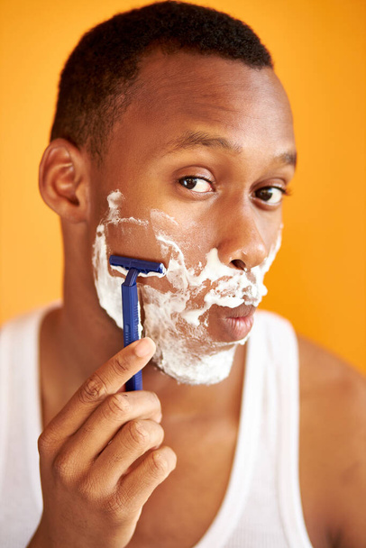 black afro man shaving his face with the razor blade through shave foam - 写真・画像