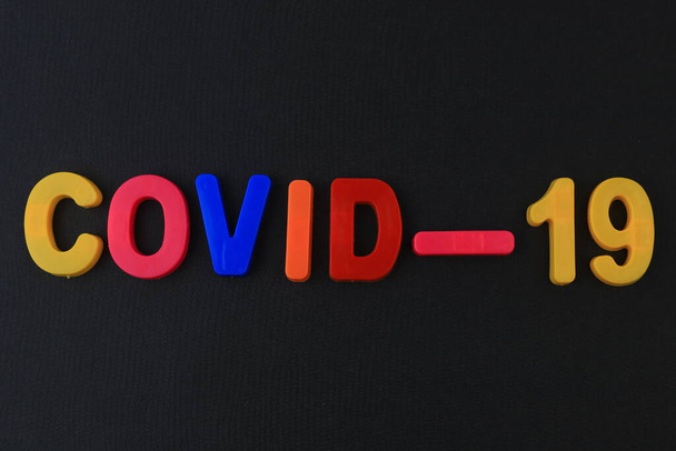 Een woord of tekst Covid-19 geschreven in een kinderalfabet met klassieke letters op een magneet. - Foto, afbeelding