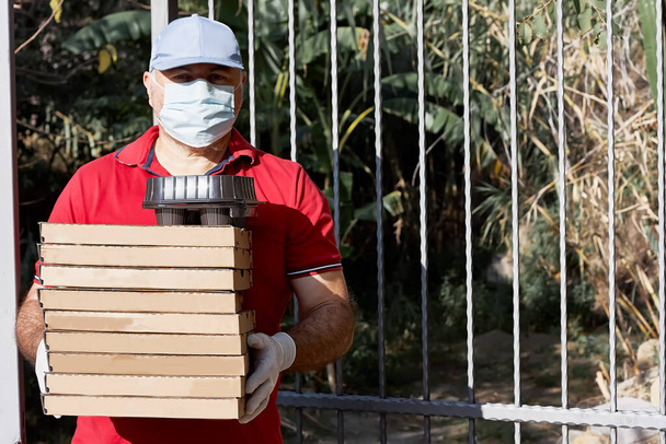Service de livraison de nourriture homme avec des cartons de pizza et emporter tasses à café entre dans la porte. Commande de nourriture et service de livraison. Assistance en quarantaine en raison d'une infection par le coronavirus Covid-19 - Photo, image