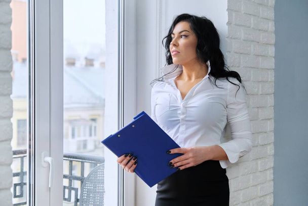 Portrait of beautiful businesswoman with business folder in office near window - Φωτογραφία, εικόνα
