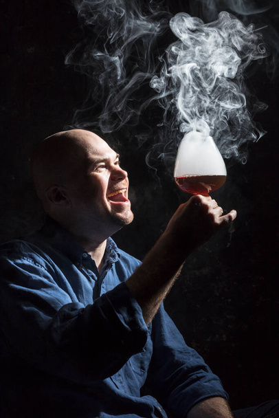 Solid bald man in shirt with glass of whisky and fume - Photo, image