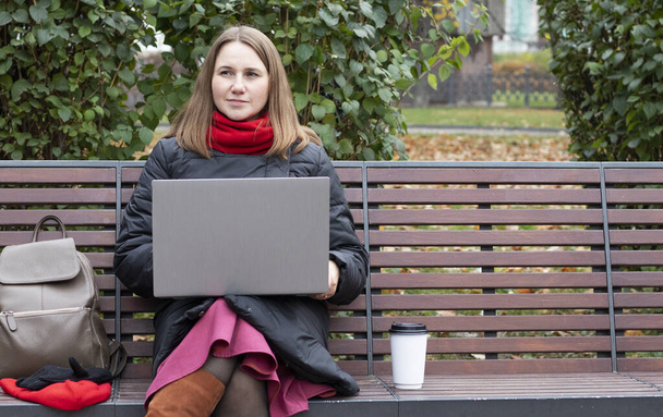giovane donna si siede su una panchina del parco e lavora in un computer per strada. - Foto, immagini