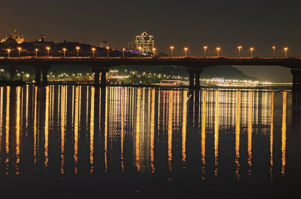 Prachtige landschapsfoto van Kiev 's nachts. Beroemde Paton brug over de rivier Dnipro. Spiegelreflecties op glad water van de rivier. Lange tijd blootgesteld. Mooie herfstavond. Kiev, Oekraïne. - Foto, afbeelding