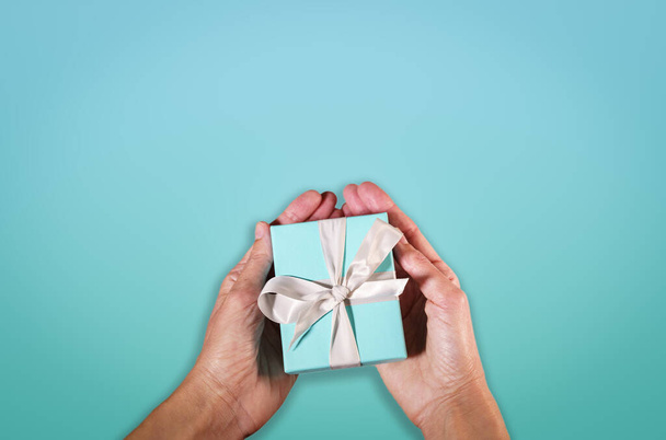 handen met een turquoise geschenkdoos gebonden met wit satijnen lint - Foto, afbeelding