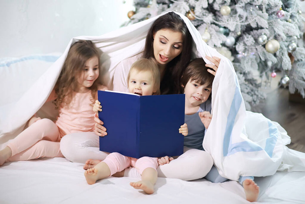 Rodzina z dziećmi bawiącymi się na łóżku pod kołdrą podczas świąt Bożego Narodzenia. - Zdjęcie, obraz