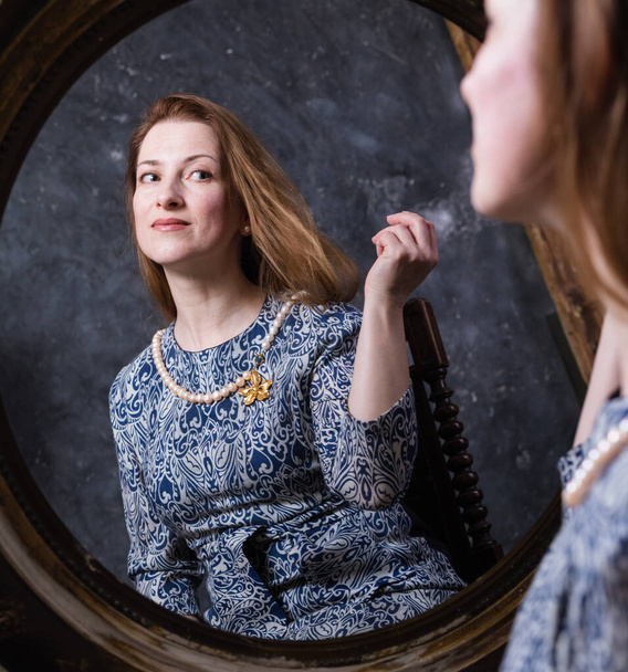 Cheerful middle aged woman looks in vintage style mirror - Foto, afbeelding