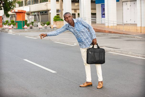 joven hombre de negocios de pie junto a la carretera haciendo señas a un coche . - Foto, Imagen