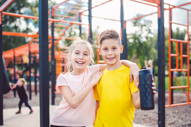 Teens children and sports theme. Two kids athletes twins rest and replenish their thirst during workout outdoor gym workout in sunny summer weather. Sporty twin. Siblings posing on street gym. - Photo, Image